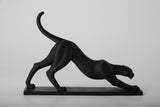 Stretching panther sculpture styled on a wooden shelf alongside books and ceramic objects