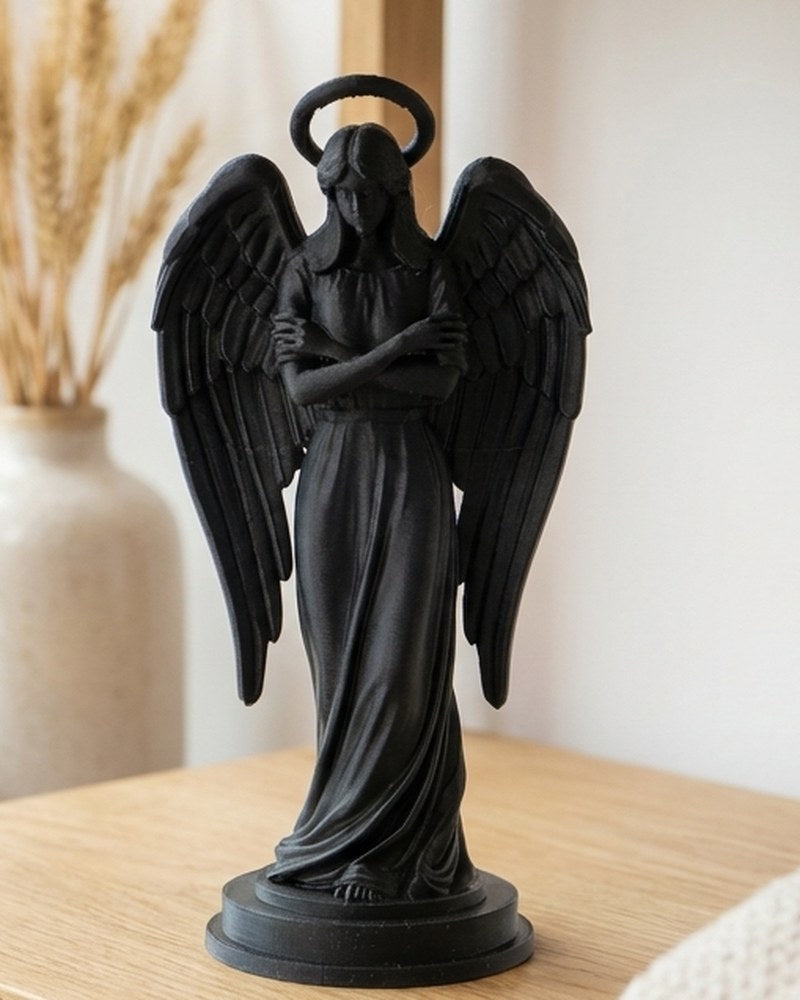 Matte black angel figurine with outstretched wings on a white surface, close-up view