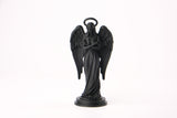Angel figurine styled on a dark wood shelf with candles and dried botanicals