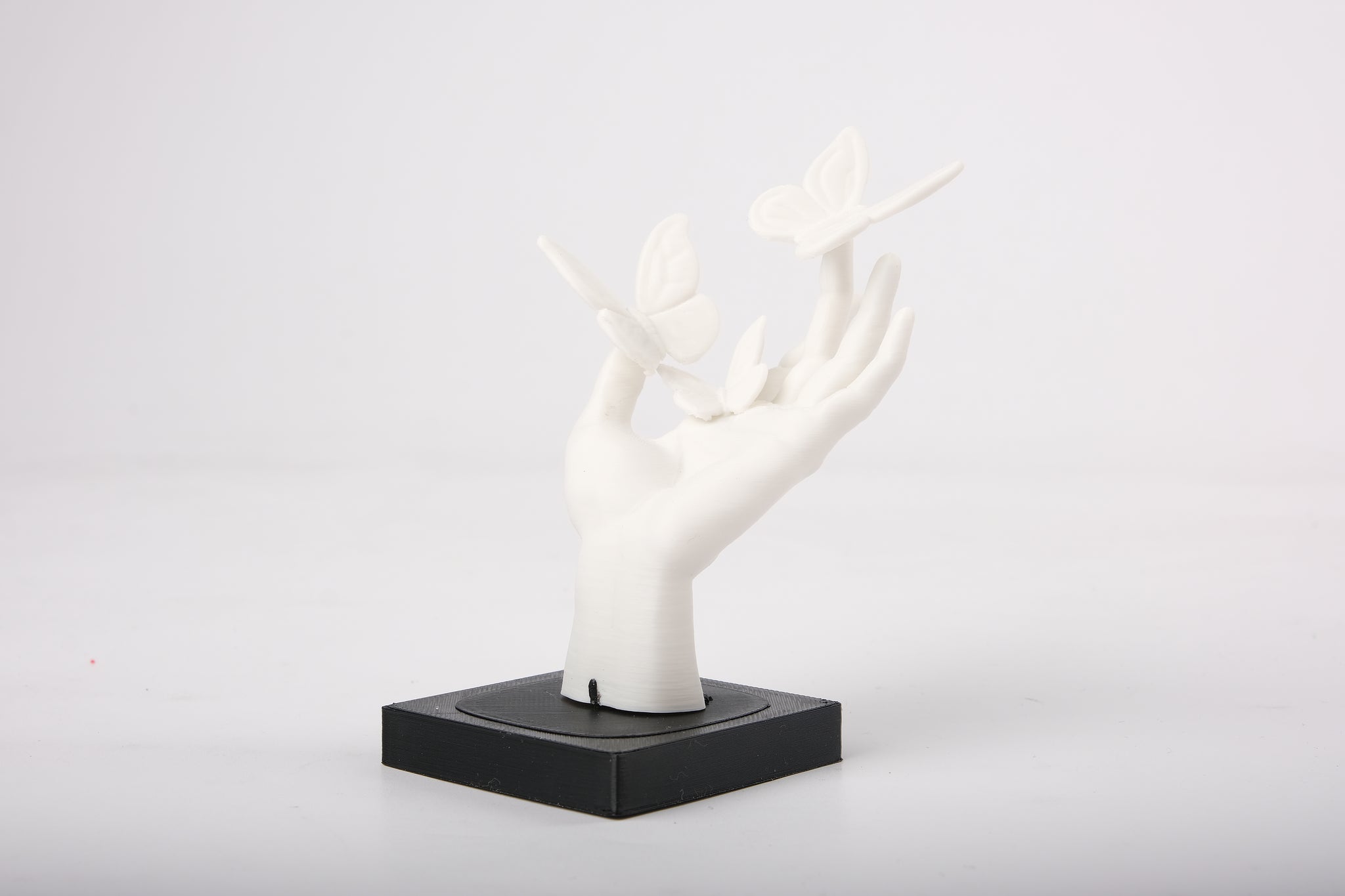 Butterfly hand sculpture styled on a minimalist wooden shelf alongside a small ceramic vase