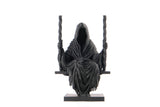 Dark gothic grim reaper sculpture styled on a dark wooden shelf with candles and moody decor