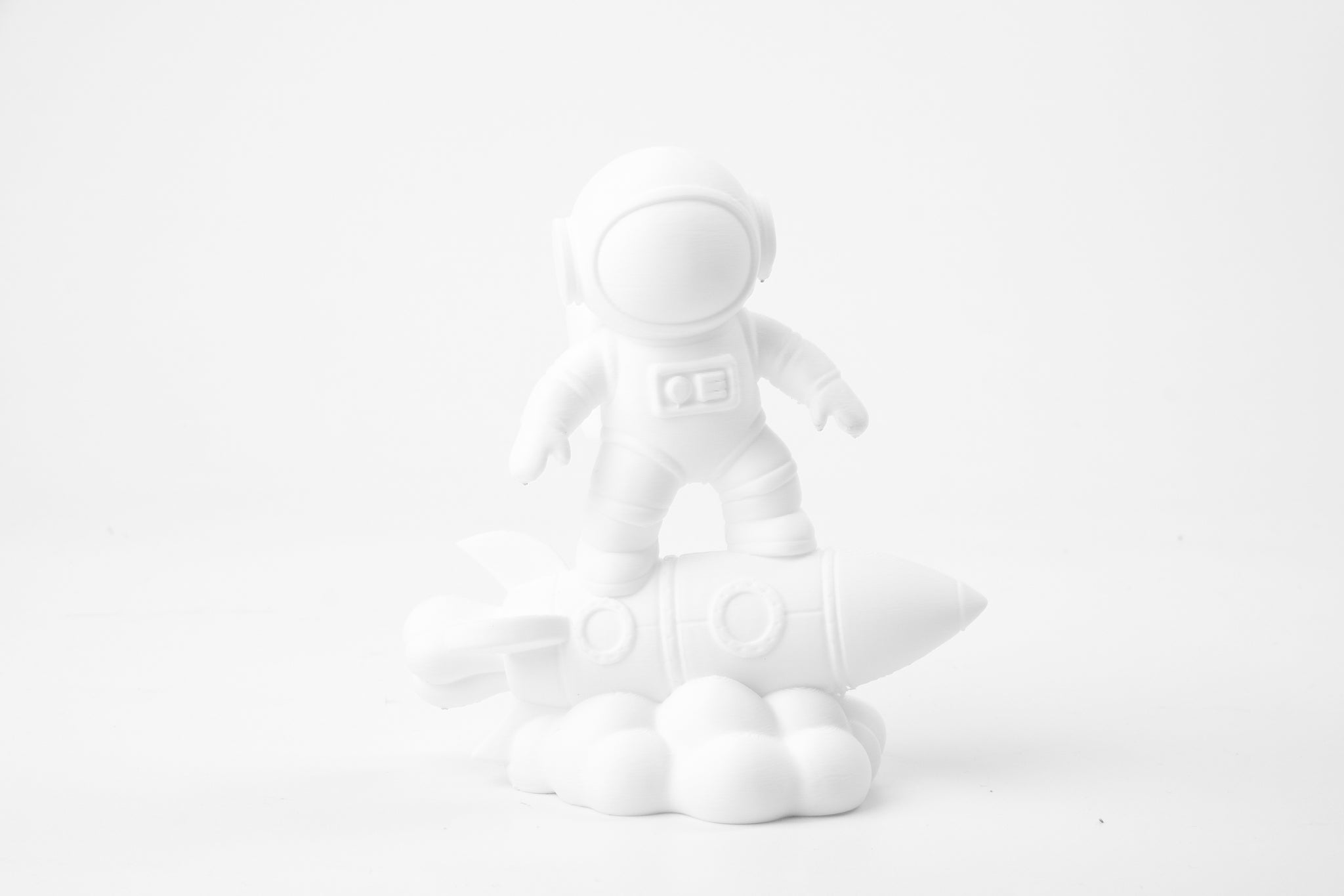 Astronaut on rocket sculpture styled on a minimal desk beside a plant and small books