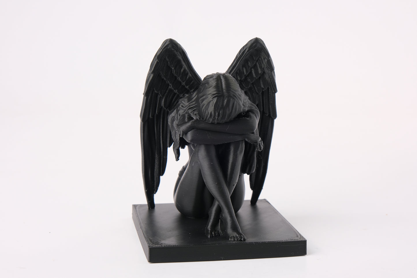 Crying angel sculpture styled on a dark wooden shelf beside a candle and dried botanicals