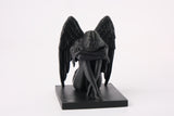 Crying angel sculpture styled on a dark wooden shelf beside a candle and dried botanicals
