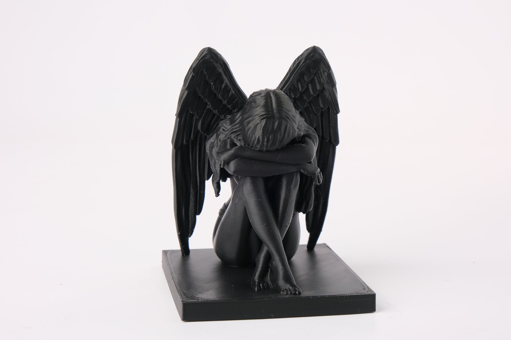 Crying angel sculpture styled on a dark wooden shelf beside a candle and dried botanicals