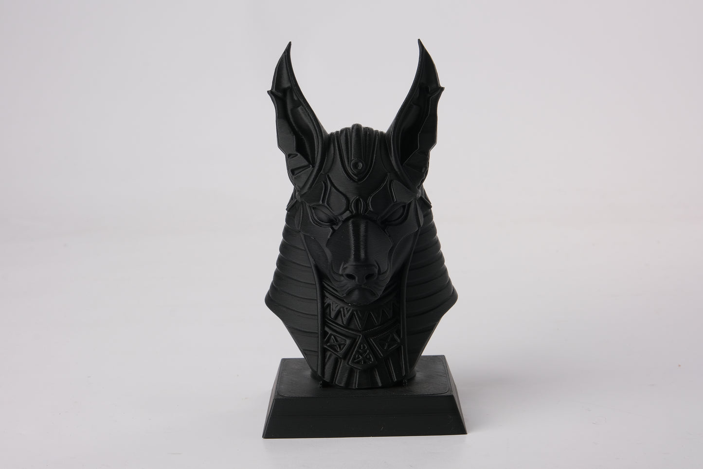 Anubis bust styled on a dark wooden shelf alongside candles and minimal decor objects