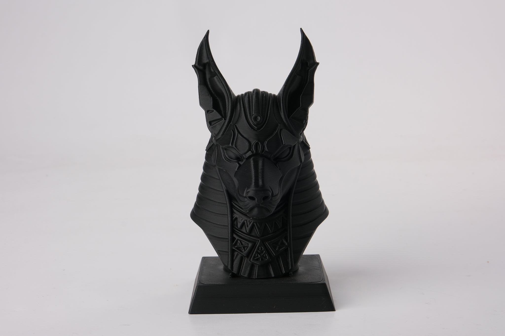 Anubis bust styled on a dark wooden shelf alongside candles and minimal decor objects