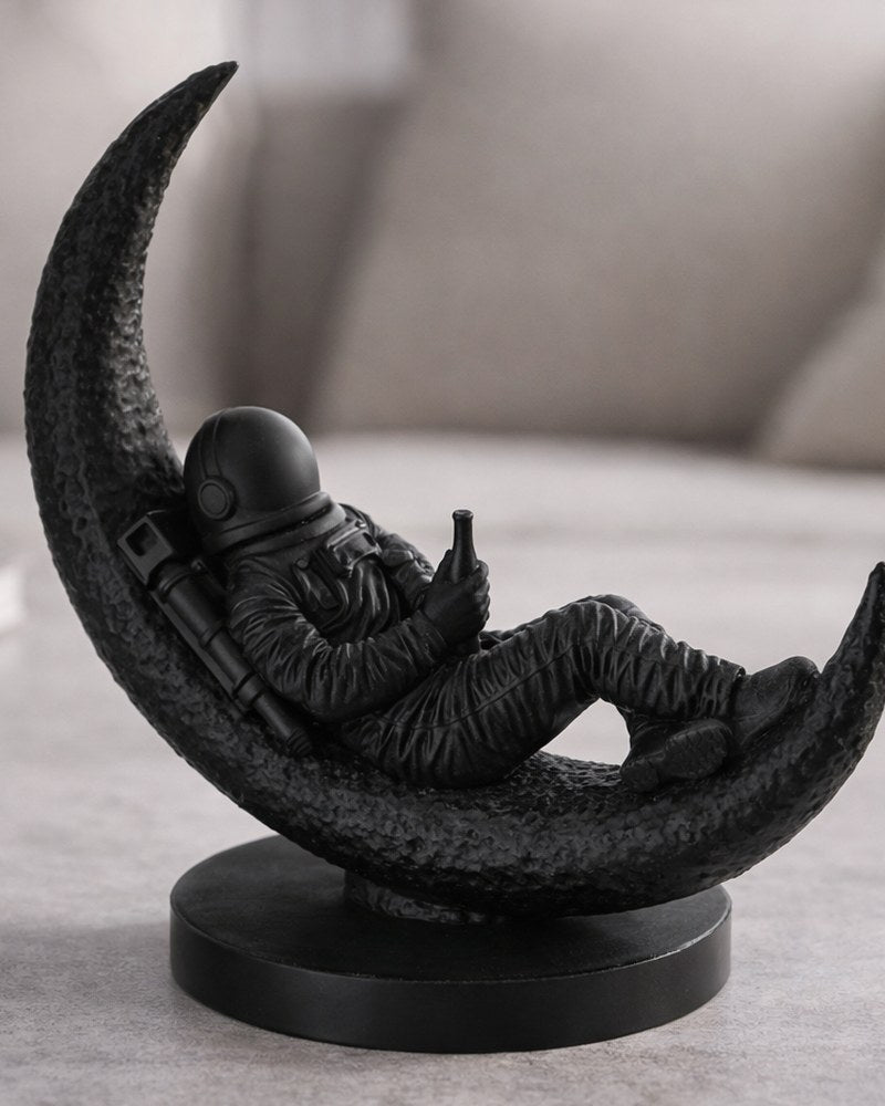 Astronaut sculpture seated on crescent moon, matte surface, close-up on white background