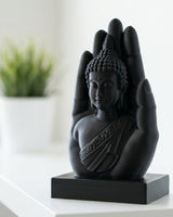 Matte black buddha hand sculpture on a white surface, close-up view showing serene figure resting in open palm