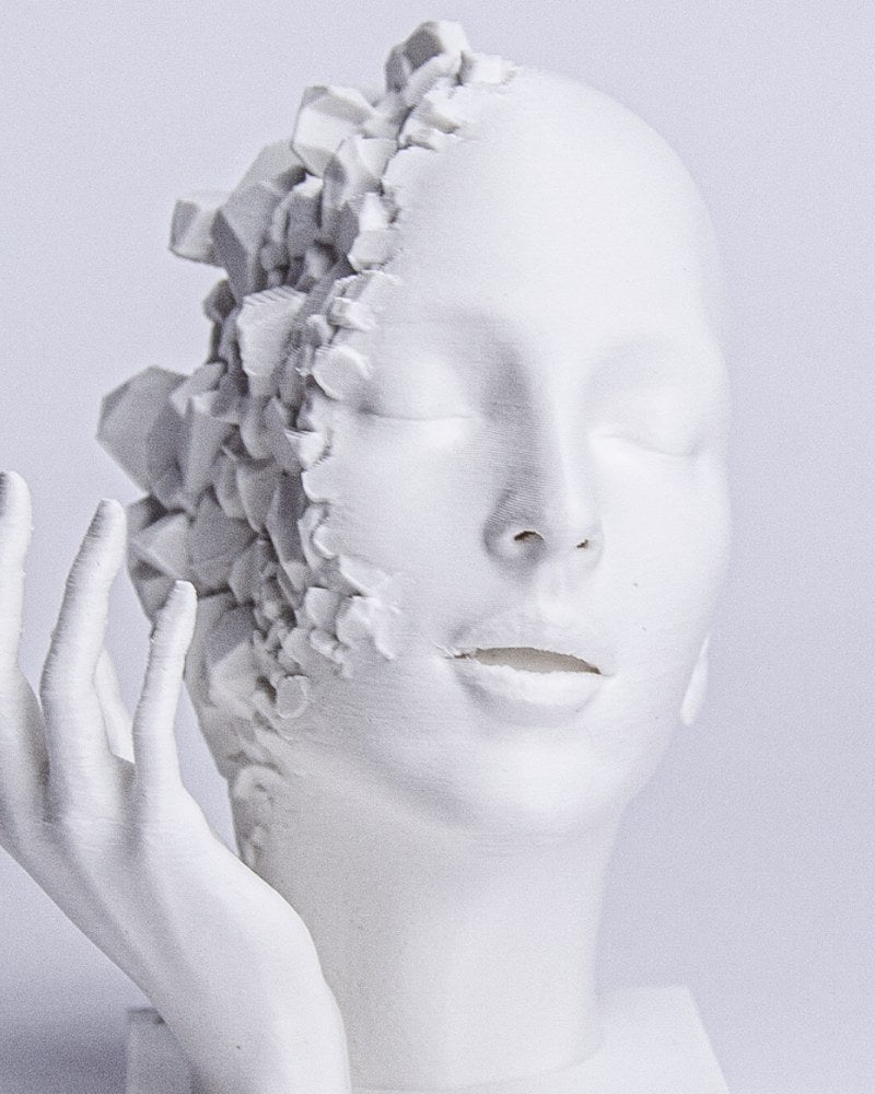 Close-up of shattered face sculpture showing geometric fragmentation and calm facial expression