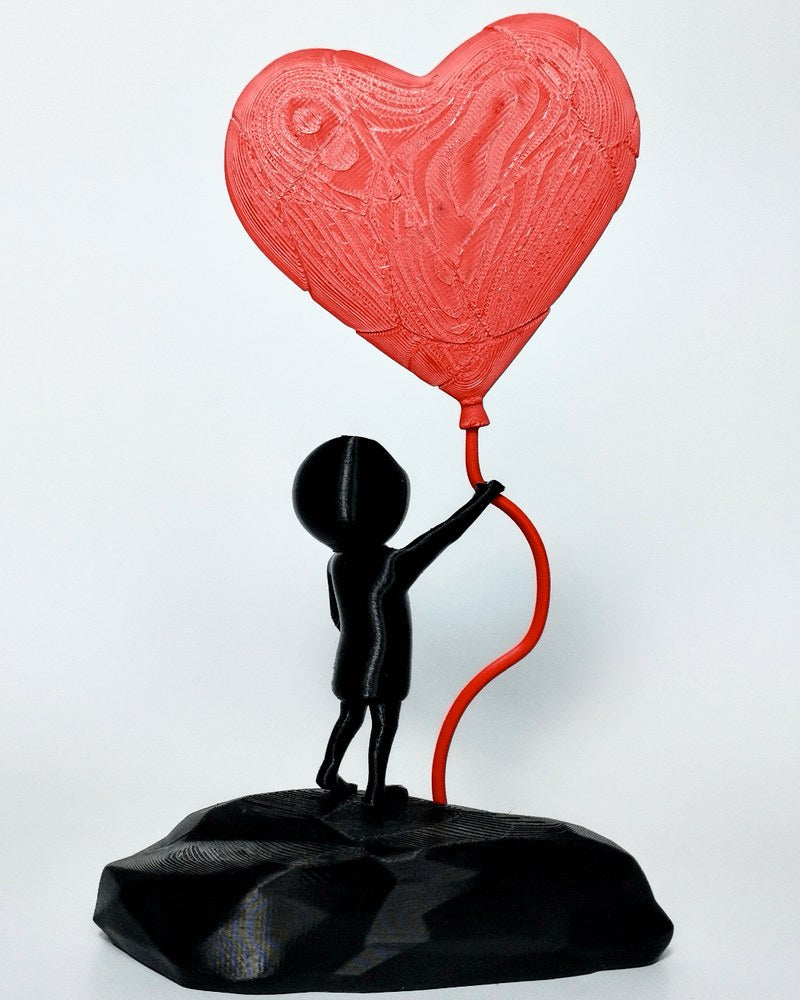Close-up of heart balloon boy sculpture, black figure holding red heart balloon against white background