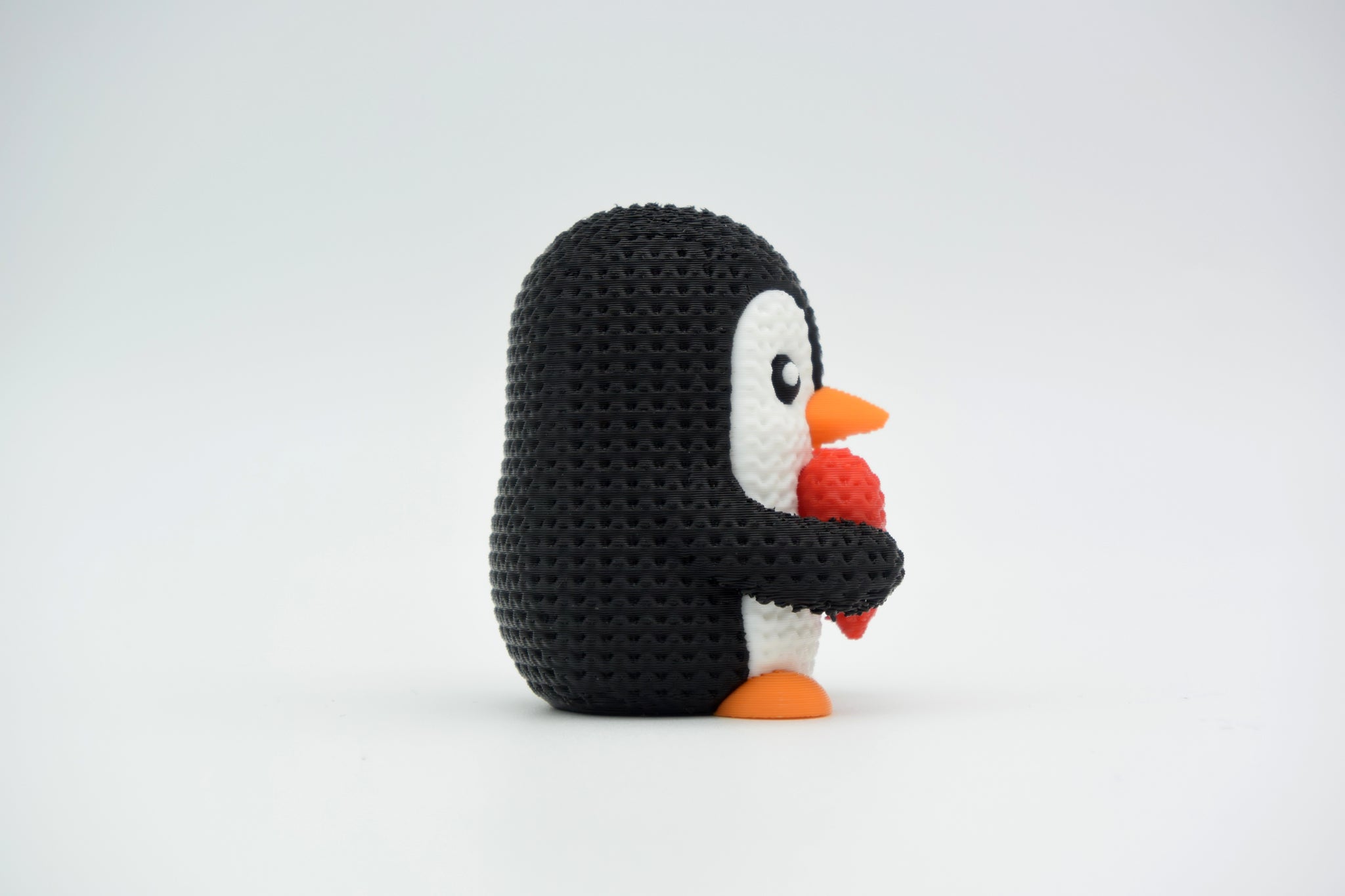 Knitted valentine penguin styled on a wooden shelf beside a candle and dried flowers