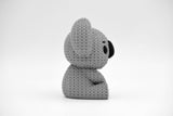 Small knitted koala decoration placed on a light wooden shelf beside a plant in a Scandinavian home interior