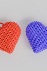 Close-up of a double-sided knitted heart keychain showing soft woven texture on both faces, in warm red