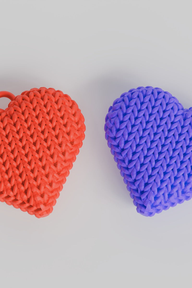 Close-up of a double-sided knitted heart keychain showing soft woven texture on both faces, in warm red