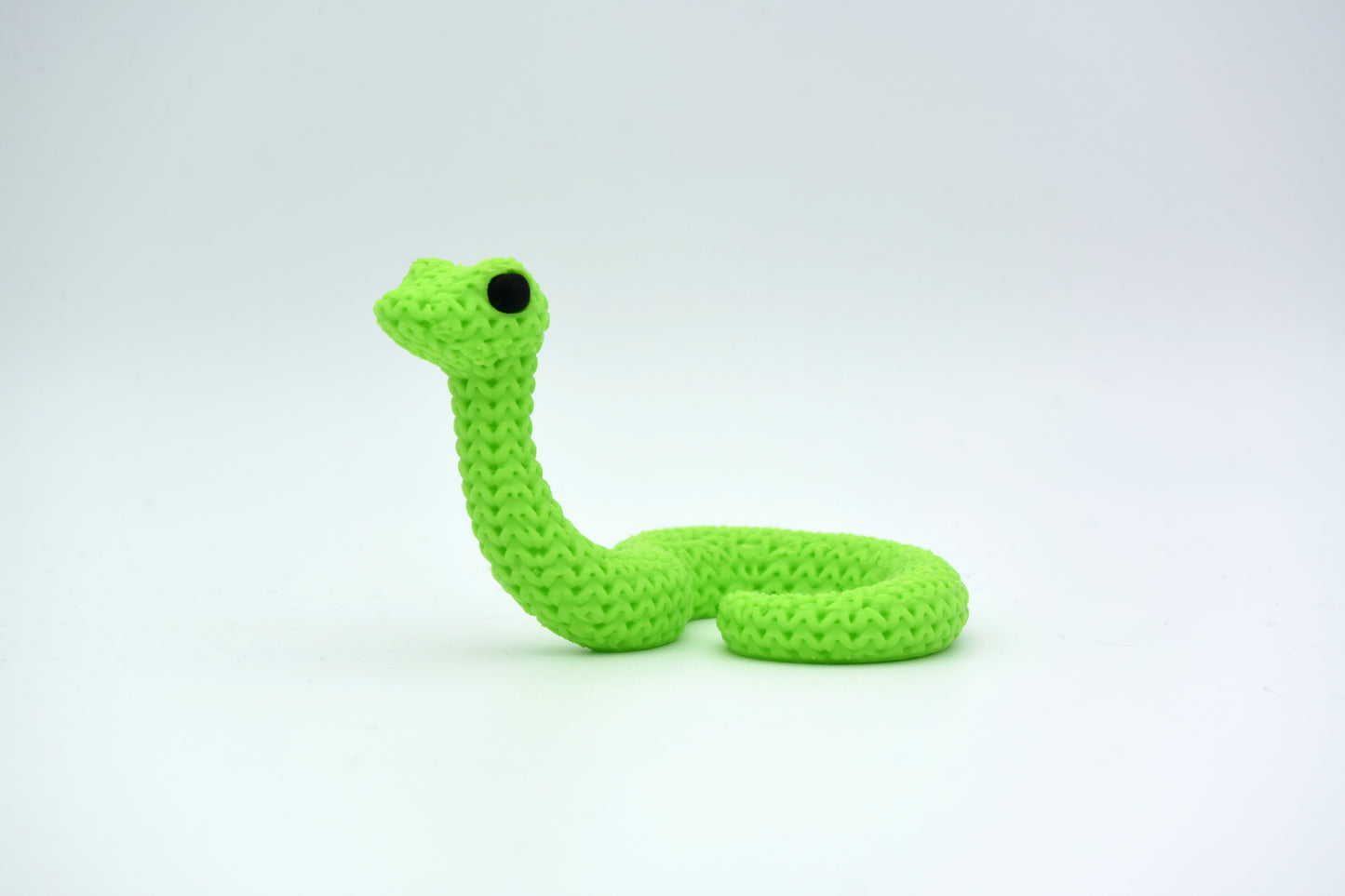 Small knitted snake decoration placed on a wooden shelf beside plants and books in a Scandinavian home setting