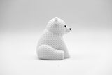 Knitted polar bear figurine styled on a light wooden shelf next to a small plant and neutral home decor