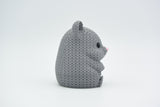 A decorative knitted hamster sitting on a wooden shelf beside a small plant in a Scandinavian home interior