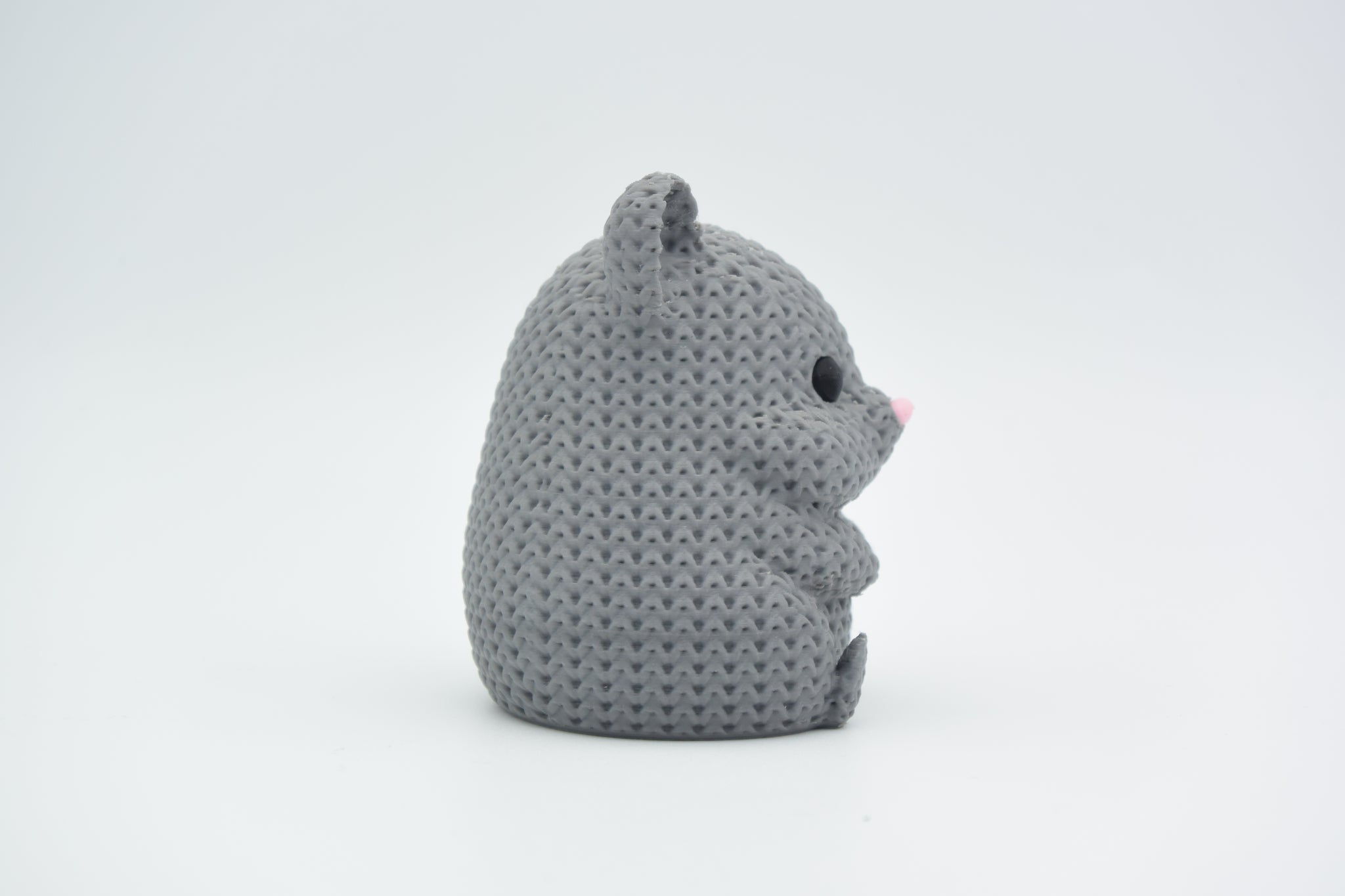 A decorative knitted hamster sitting on a wooden shelf beside a small plant in a Scandinavian home interior