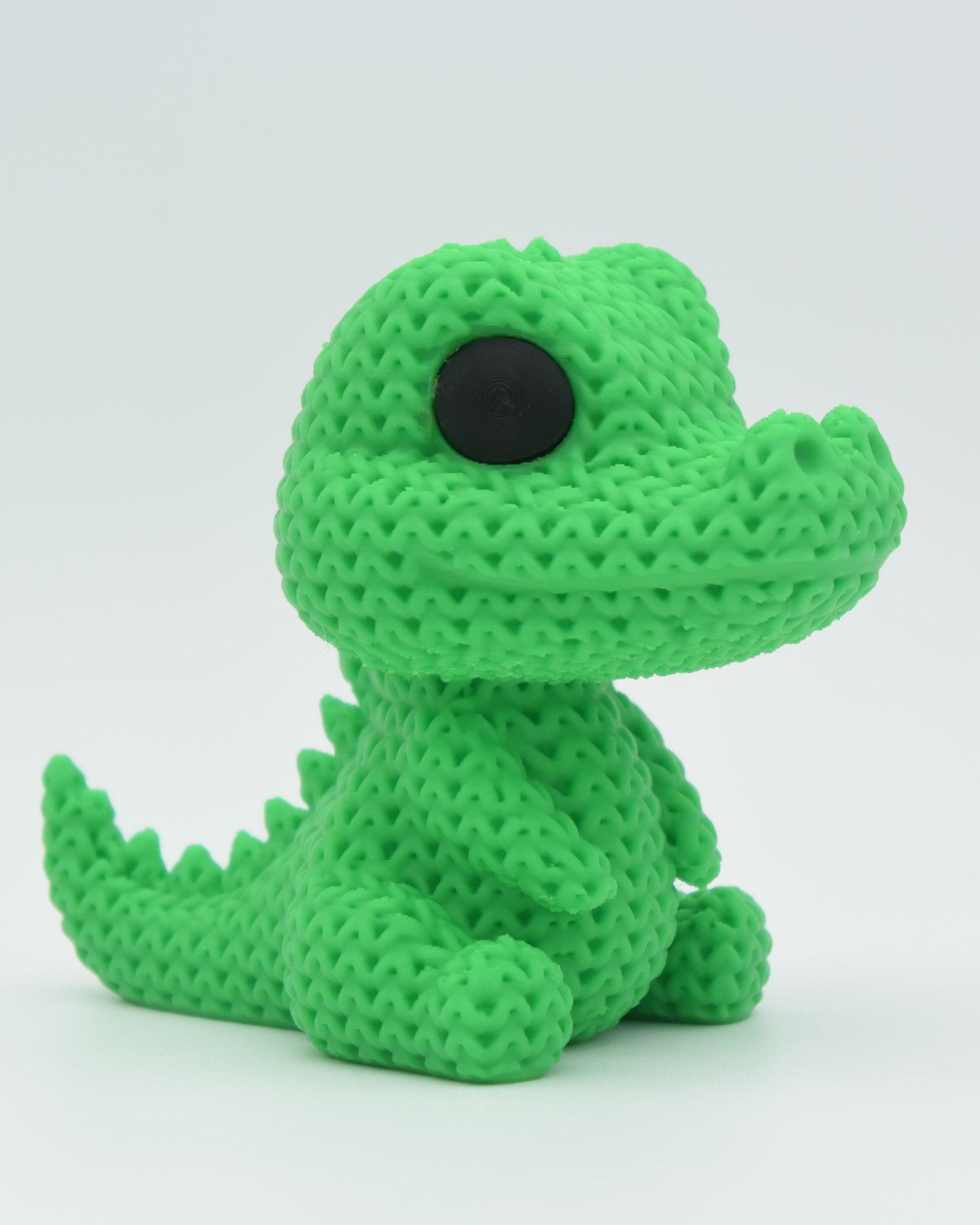 Close-up of a knitted crocodile decoration with textured crochet-look surface and small round eyes, 80mm long