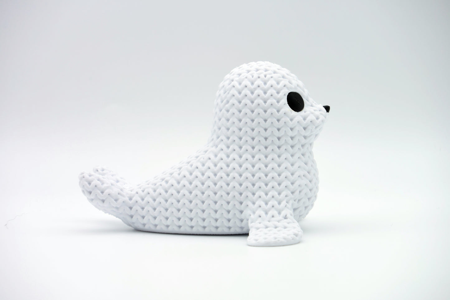 Knitted seal figure styled on a wooden shelf beside small plants and books in a Scandinavian home interior