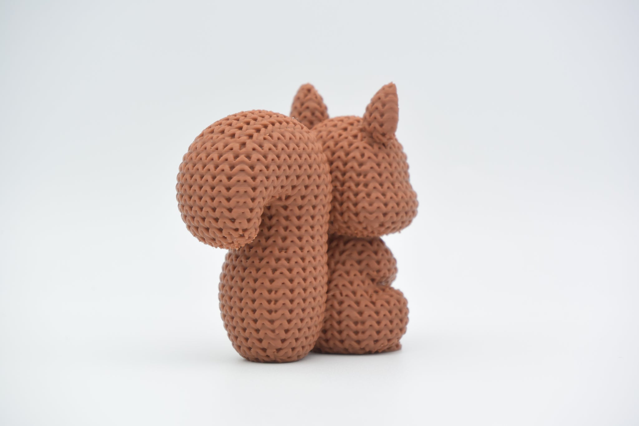 Knitted squirrel decorative figure styled on a wooden shelf next to books and a small potted plant