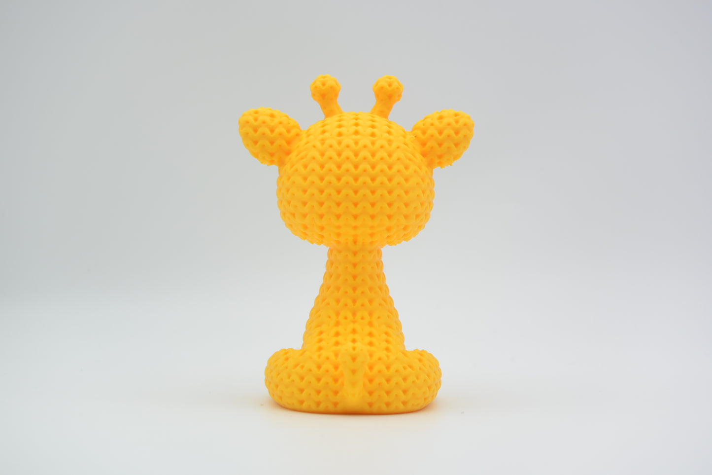 Close-up of a small knitted giraffe figurine with crochet-textured surface and expressive eyes, approx 8 cm tall