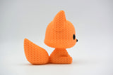 Small knitted fox figurine styled on a wooden shelf next to books and a plant in a Scandinavian home
