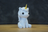 Knitted unicorn figurine styled on a wooden shelf beside small plants and soft home decor objects