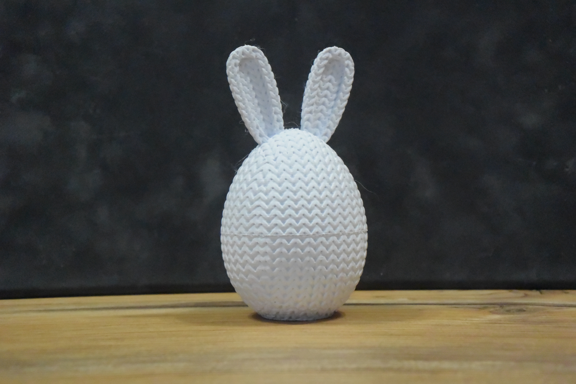 Knitted Easter egg container with bunny ears in pastel pink, standing upright on a white surface, close-up view