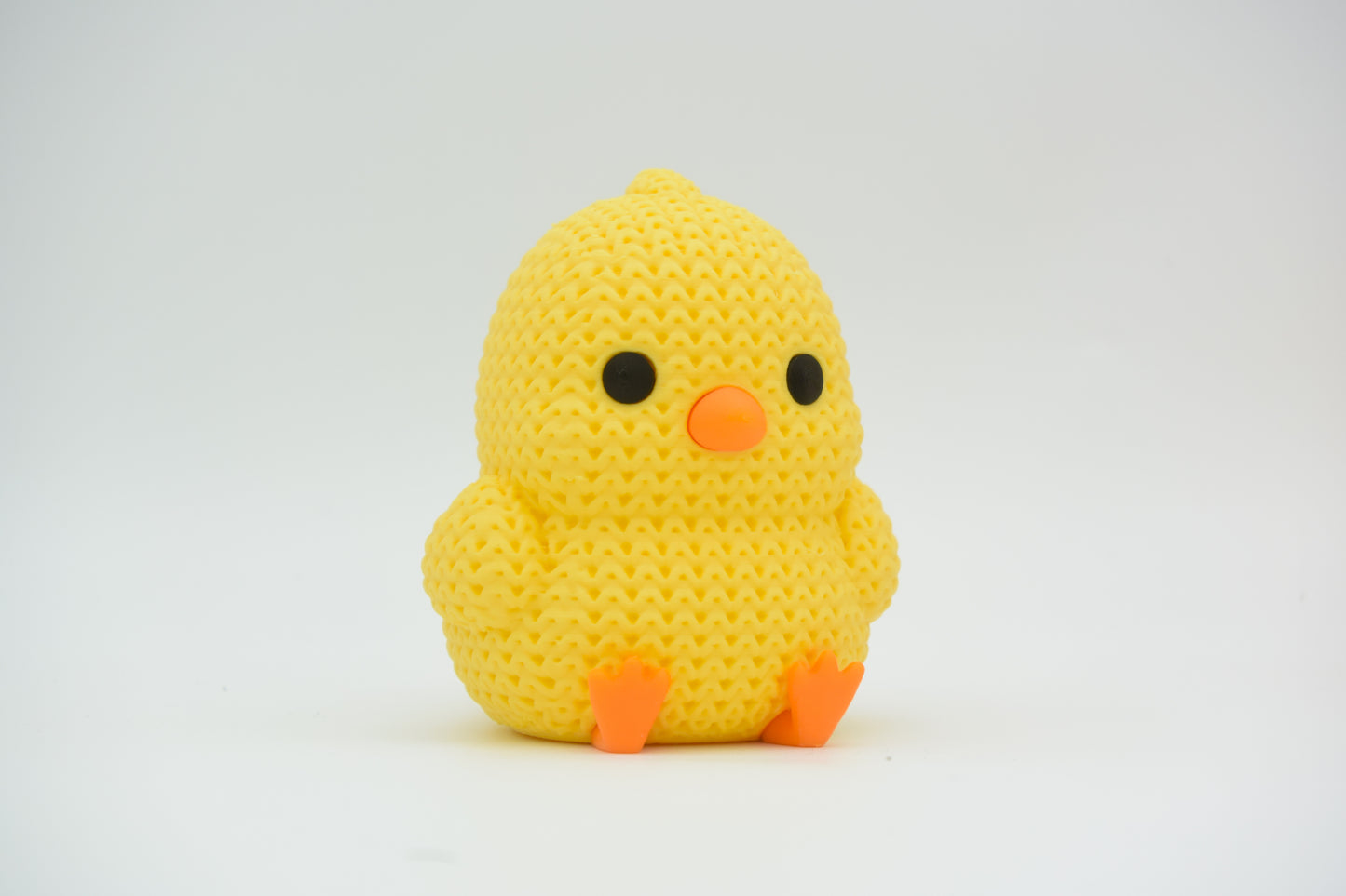 Close-up of a small knitted chick decoration with crochet texture, yellow with orange beak and feet
