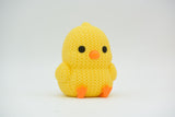 Close-up of a small knitted chick decoration with crochet texture, yellow with orange beak and feet
