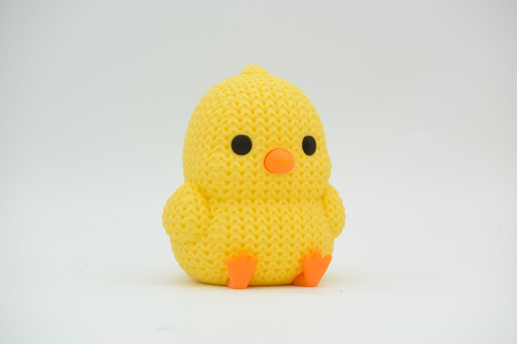 Close-up of a small knitted chick decoration with crochet texture, yellow with orange beak and feet