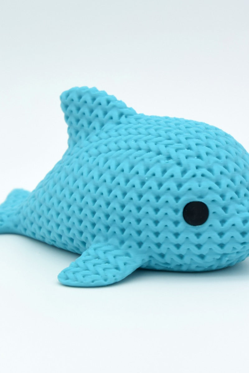 Close-up of a small knitted dolphin figurine with soft crochet-textured surface and round inset eyes
