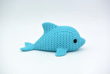 Knitted dolphin decoration placed on a wooden shelf beside coastal home accessories and a small plant