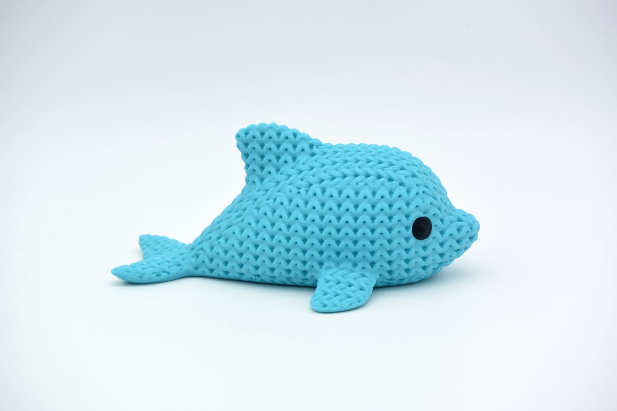 Knitted dolphin decoration placed on a wooden shelf beside coastal home accessories and a small plant
