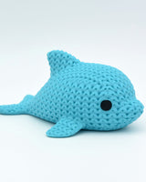 Close-up of a small knitted dolphin figurine with soft crochet-textured surface and round inset eyes
