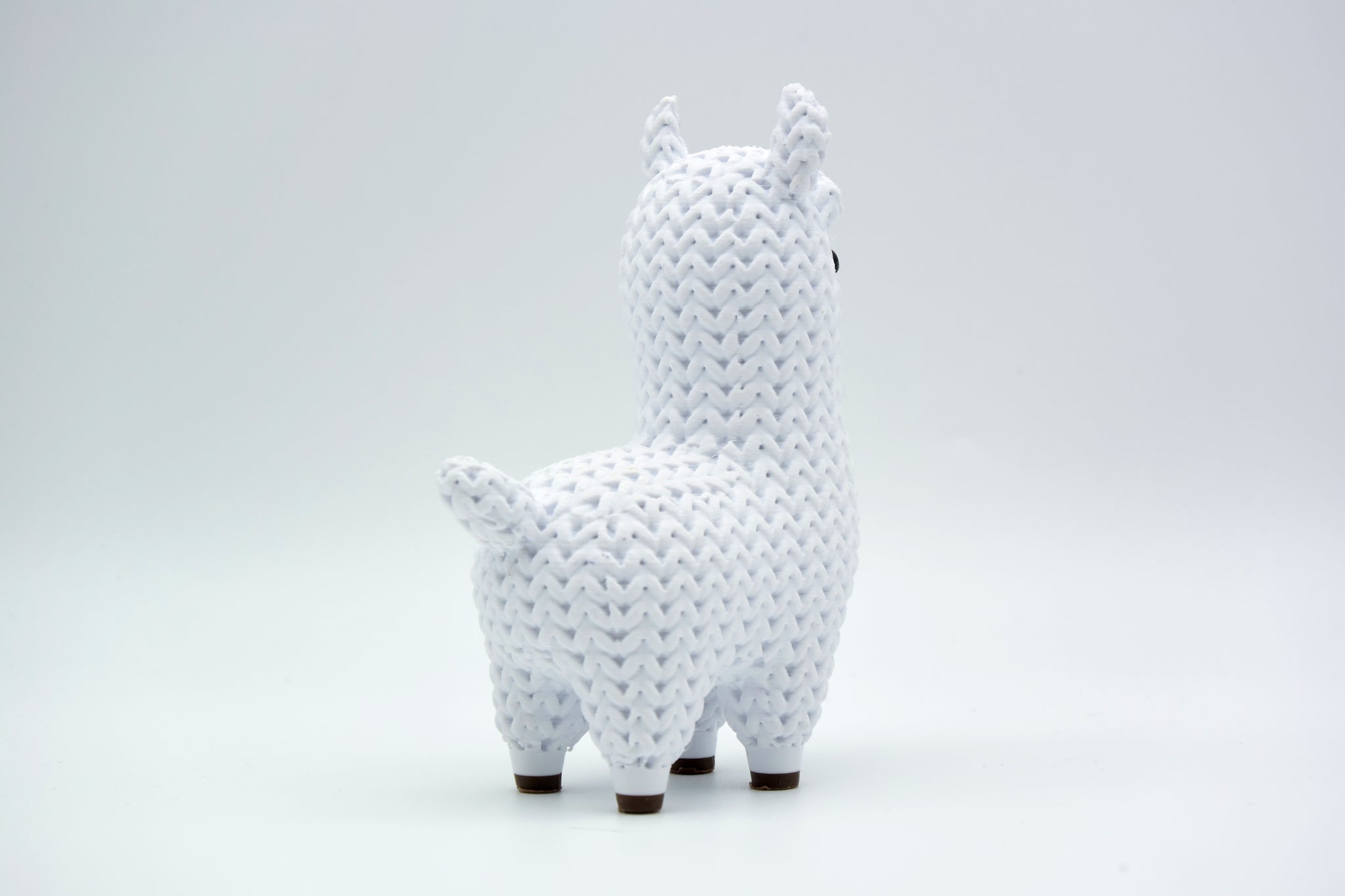 Knitted llama decorative figure styled on a wooden shelf next to a small plant and books