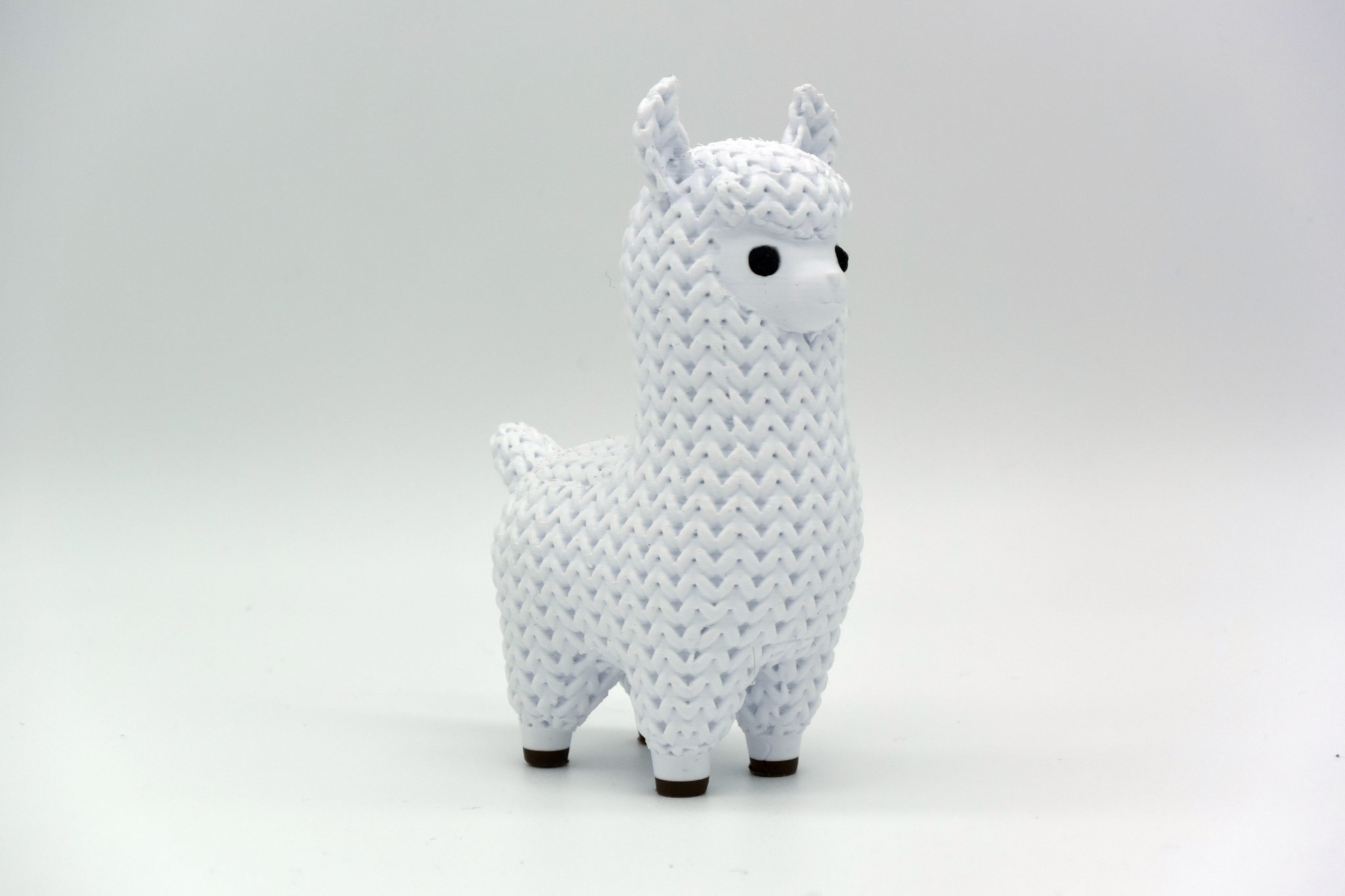 Close-up of a knitted llama figurine with soft crochet-look texture, shown in a neutral cream colour