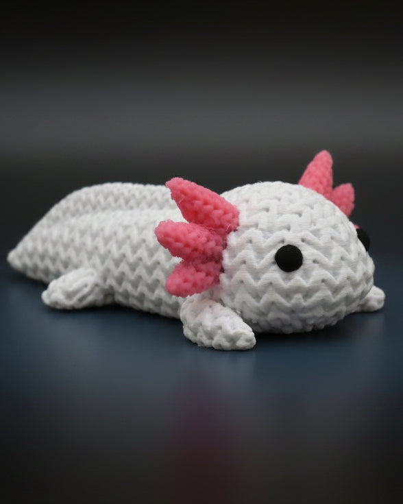 Small knitted axolotl figurine styled on a wooden shelf beside books and a plant in a Scandinavian interior