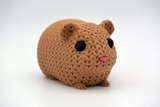 Small knitted guinea pig figurine placed on a wooden shelf next to books and a potted plant
