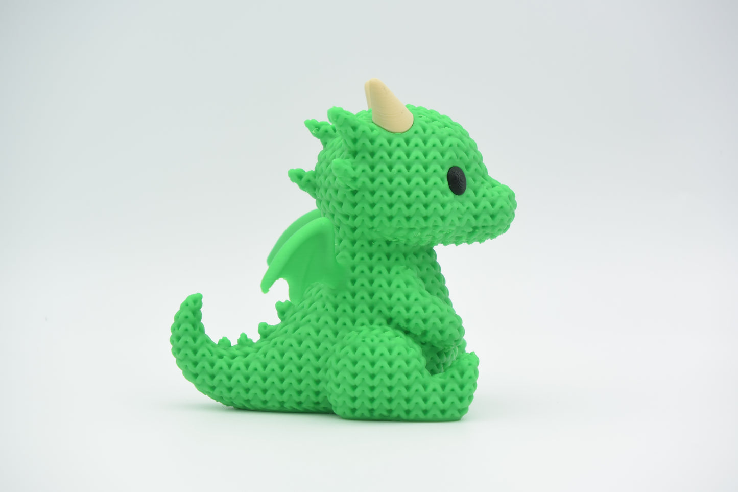 Small knitted dragon displayed on a wooden bookshelf beside books and a plant in a cosy home setting
