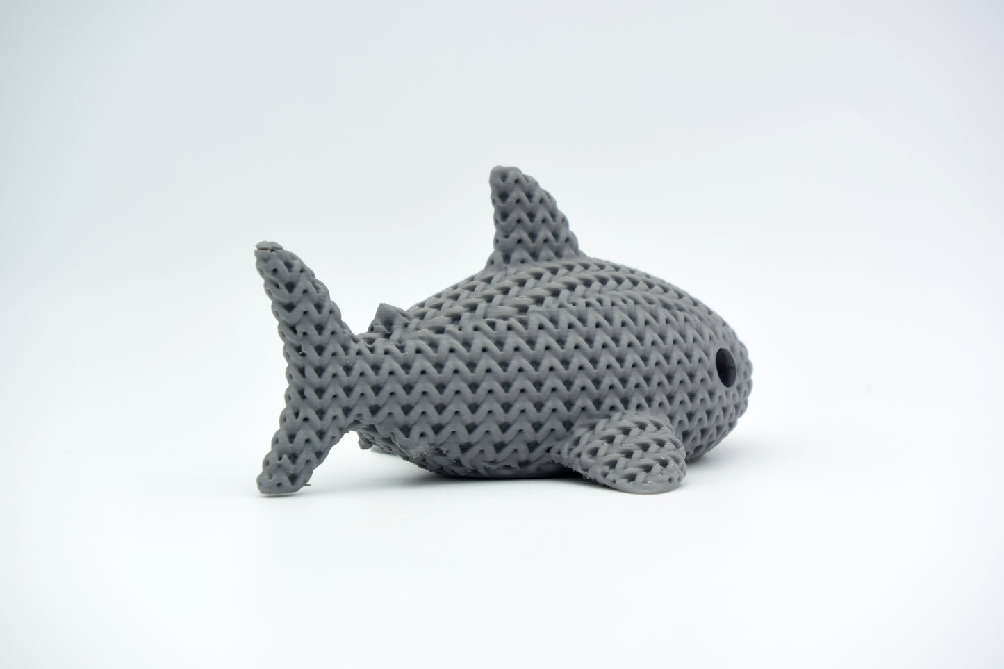 Knitted shark decoration placed on a wooden shelf beside books and small plants in a Scandinavian interior