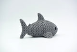 Knitted shark decoration placed on a wooden shelf beside books and small plants in a Scandinavian interior