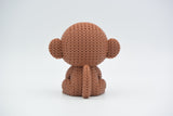 Small knitted monkey figure styled on a wooden shelf beside books and a green plant