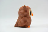 Small knitted owl decoration styled on a wooden shelf next to books and a green plant in a Scandinavian living room