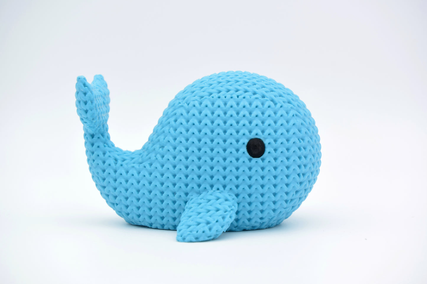 A knitted whale decorative figurine styled on a wooden shelf beside sea-toned home accessories