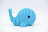 A knitted whale decorative figurine styled on a wooden shelf beside sea-toned home accessories