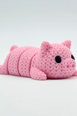 Close-up of a knitted pig keychain with crochet texture and small black eyes, shown against a white background