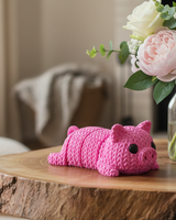 Close-up of a knitted pig keychain with crochet texture and small black eyes, shown against a white background